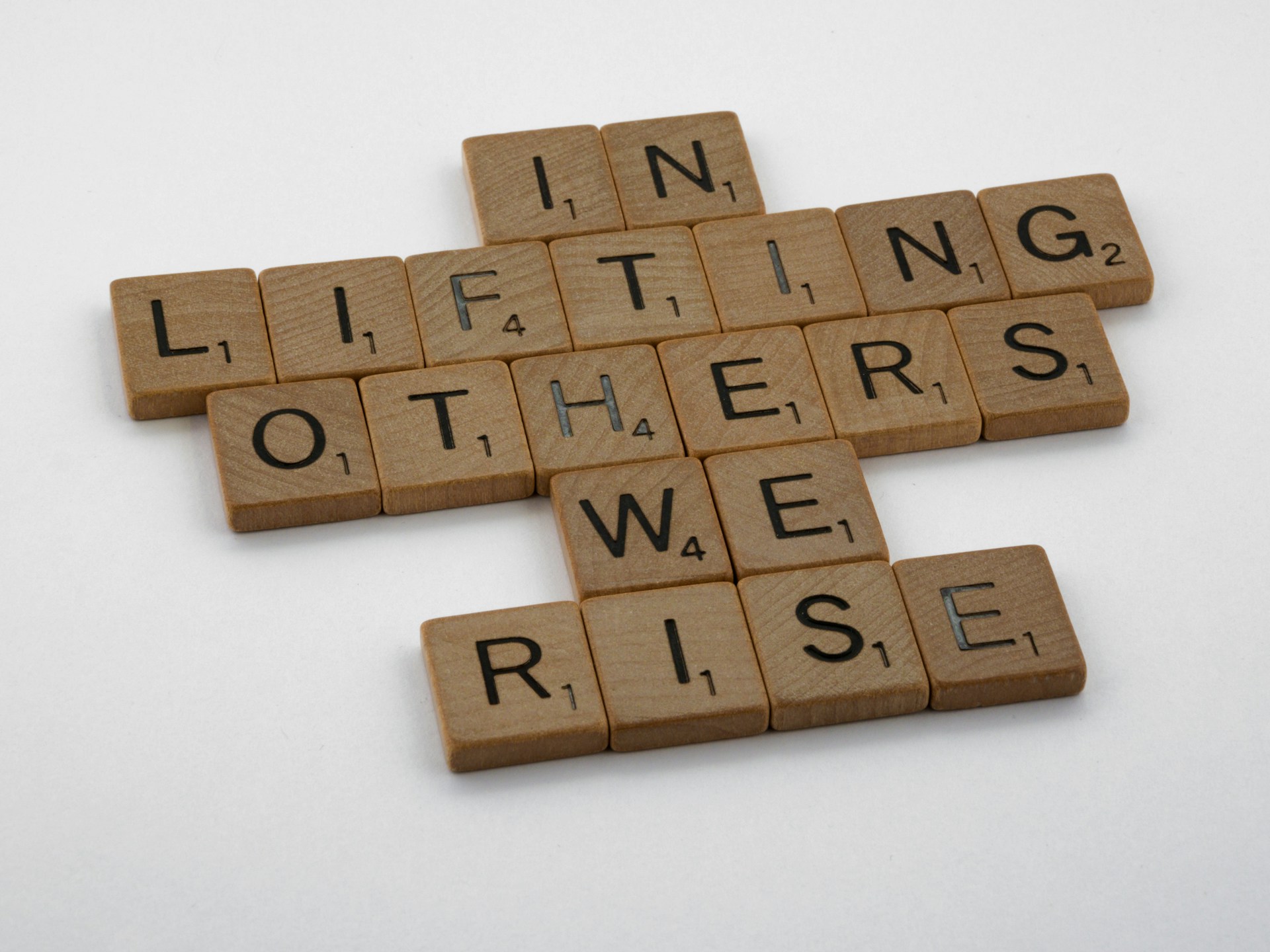 Wooden scrabble tiles read In lifting others we rise