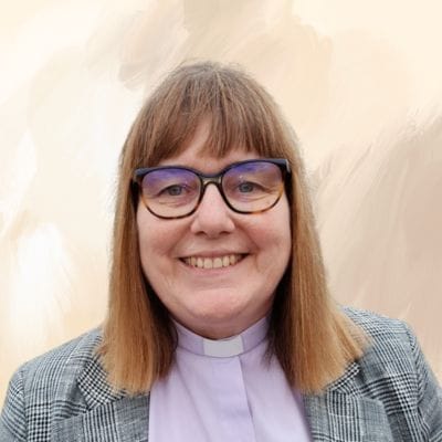 A smiling woman wearing a clerical collar and glasses, exuding warmth and approachability