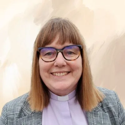 A smiling woman wearing a clerical collar and glasses, exuding warmth and approachability